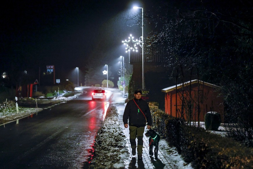 PRODUKTION - 19.12.2022, Schleswig-Holstein, Osterby: Kai Ulrich geht mit seiner Hündin &quot;Emma&quot; auf der Hauptstraße in Osterby Gassi. Das Dorf spart Strom mit einer außergewöhnlichen &quot;Li ...