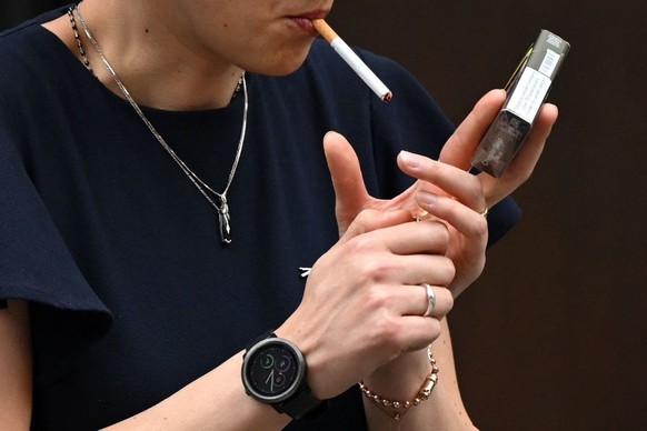 A woman is seen smoking a cigarette in central London on June 9, 2022. - The age at which people can buy tobacco in England should rise by one each year until it becomes a &quot;smoke-free&quot; socie ...