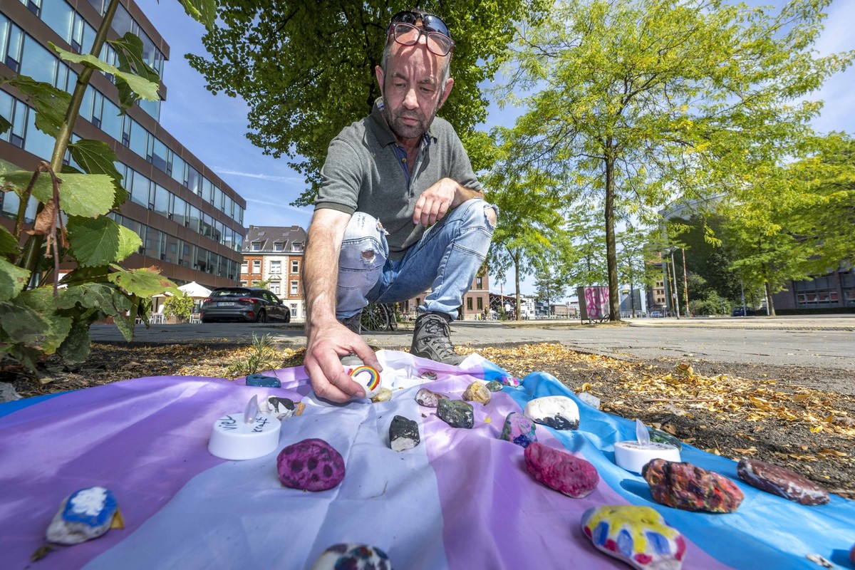 30.08.2022, Nordrhein-Westfalen, Münster: Felix Adrian Schäper vom Verein Trans*Inter*-Münster kniet vor einer Fahne mit Gedenksteinen, die Menschen auf dem Hafenplatz ausgelegt haben. Ein 25-jähriger ...