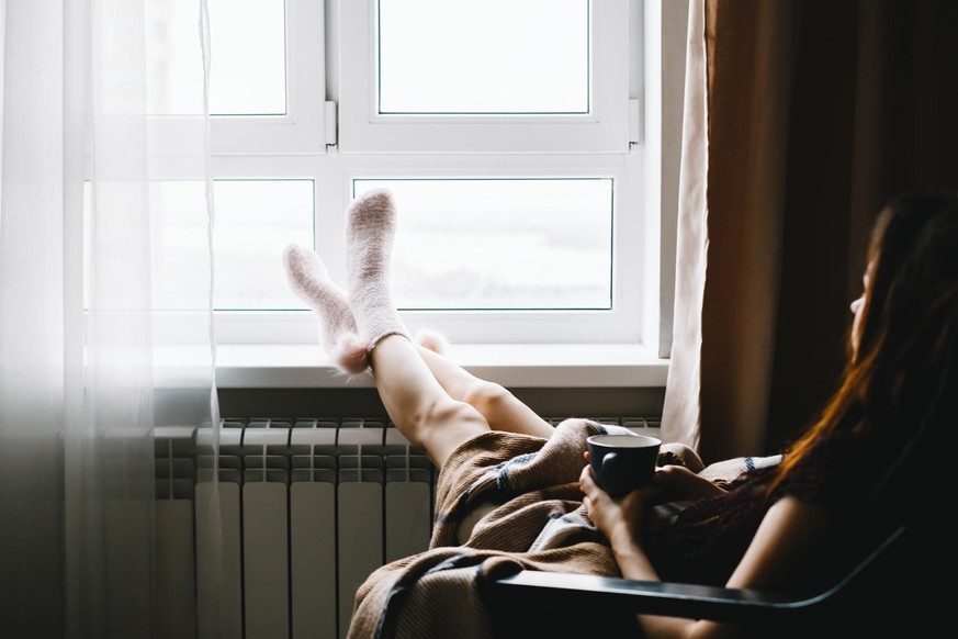 Young woman resting on armchair near the window, drinking hot tea wrapped in a blanket. High quality photo