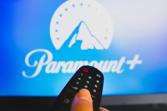 May 10, 2022, Brazil. In this photo illustration a close-up of a hand holding a TV remote control seen in front of the Paramount Plus logo. May 10, 2022, Brazil. In this photo illustration a close-up  ...