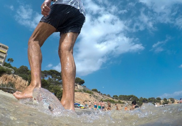 22.07.2023, Spanien, Calvia: Ein Mann spaziert am Strand von Portals Nous auf Mallorca entlang. Das Mittelmeer erwärmt sich einer Studie zufolge immer schneller und wird dabei auch immer salziger. Das ...