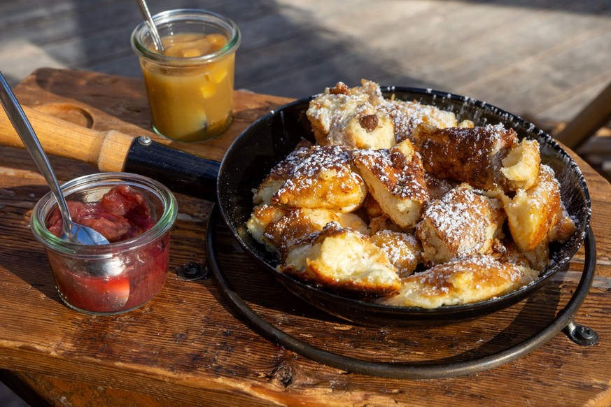 Traditioneller Wiener Kaiserschmarrn, zerkleinerte süße Pfannkuchen mit Rosinen, serviert in einer eisernen Pfanne auf alten Holzbrettern auf einem Schieferteller