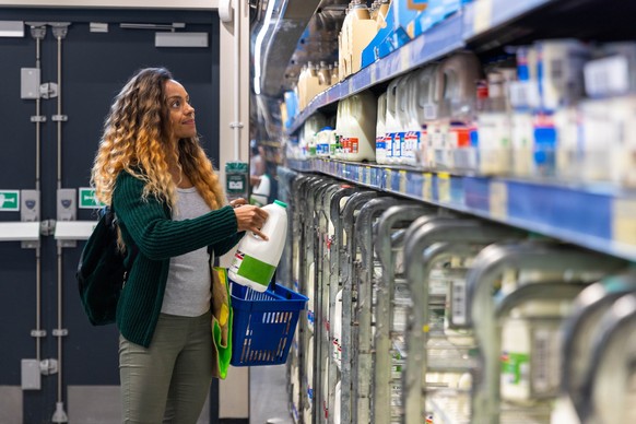 Mid-adult woman shopping on a budget. She is looking for low prices due to inflation, standing and holding a milk carton. She is living in the North East of England.