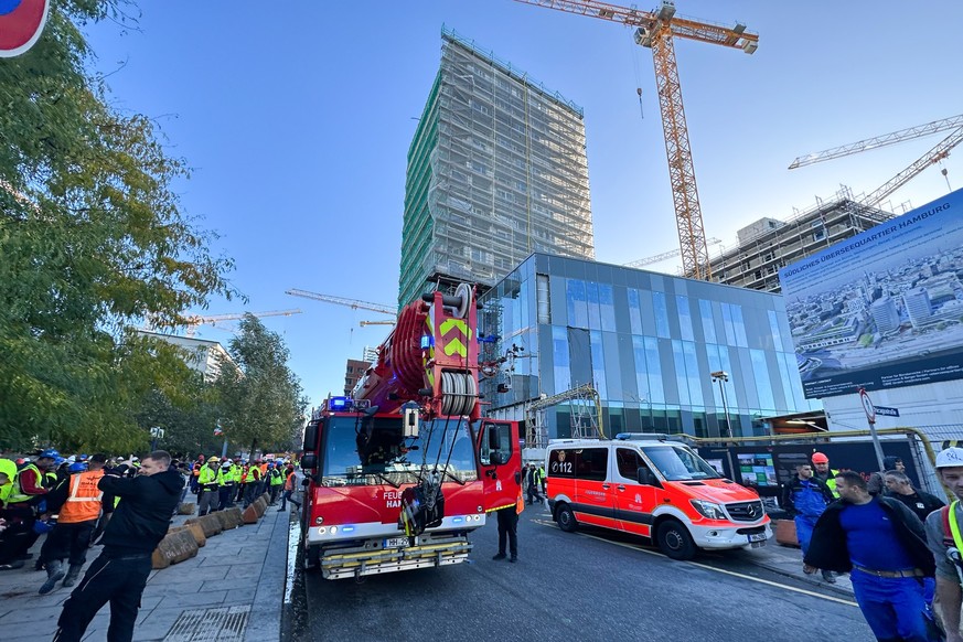 30.10.2023, Hamburg: Einsatzfahrzeuge der Feuerwehr stehen vor einem eingerüsteten Hochhaus. Auf einer Baustelle in der Hamburger HafenCity sind am Montag mehrere Arbeiter von einem Gerüst gestürzt. F ...