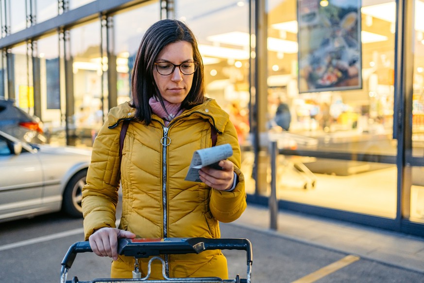 Beautiful young woman looking at the receipt from the grocery store at night, while getting out.