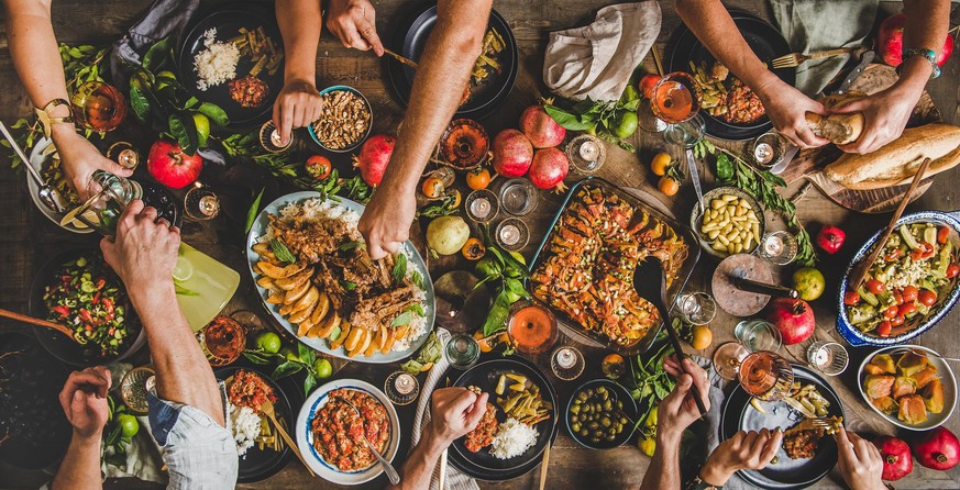 Turkish cuisine family feast. Flat-lay of peoples hands and lamb chops with quince, beans, salad, babaganush, rice pilav, pumpkin dessert, lemonade over rustic table, top view. Middle East cuisine