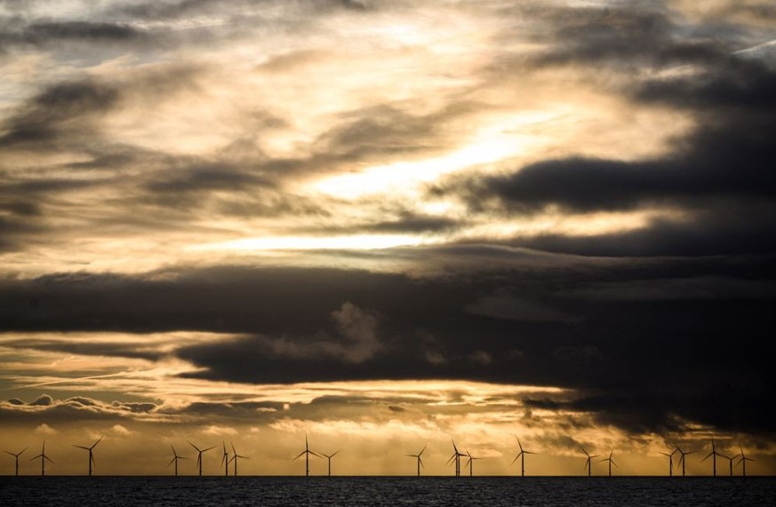 A photograph taken on January 5, 2023 from Le Pouliguen, shows the sun setting over the first offshore wind farm in France, off the coast of the French western city of Saint-Nazaire. (Photo by LOIC VE ...