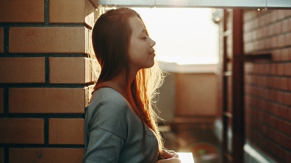 Young Woman Standing on a Street with Closed Eyes in Sunset Light. Selective Focus, Lens Flare.