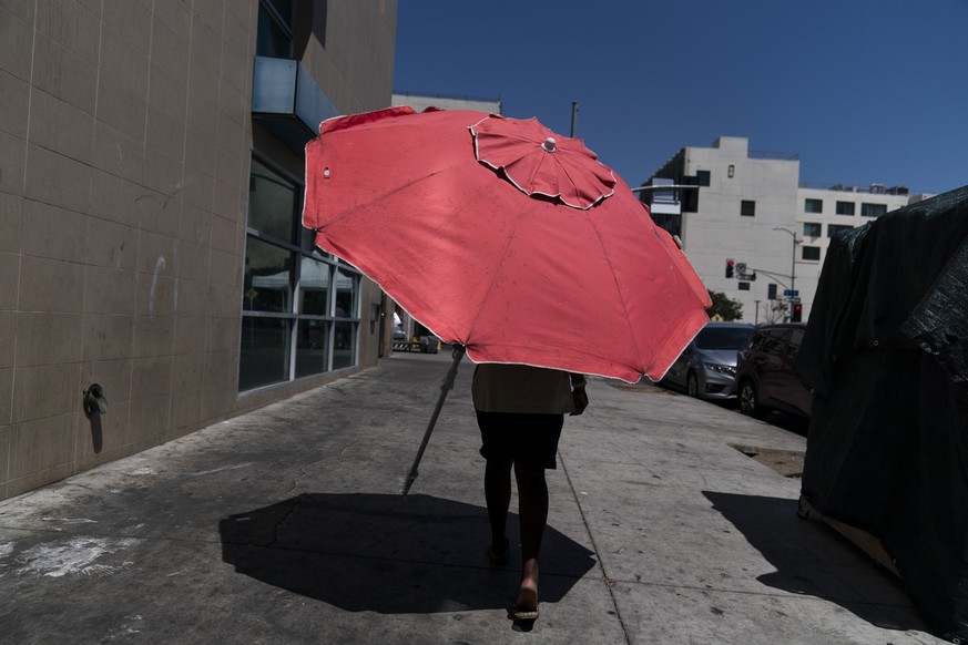 31.08.2022, USA, Los Angeles: Eine Frau geht mit einem Sonnenschirm spazieren. (zu dpa