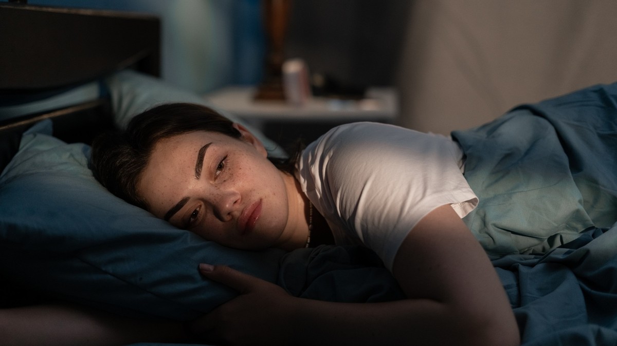 Young sad woman lying in bed late at night trying to sleep suffering insomnia. Girl in bed scared on nightmares looking worried and stressed. Sleeping disorder and insomnia concept