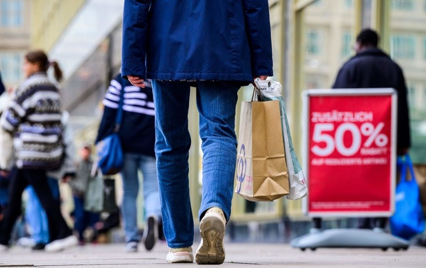 A shopper carries a bag past a sign advertising an &quot;Extra 50 percent discount on already discounted items&quot; outside a clothing retail store in Berlin on September 29, 2022. - German inflation ...