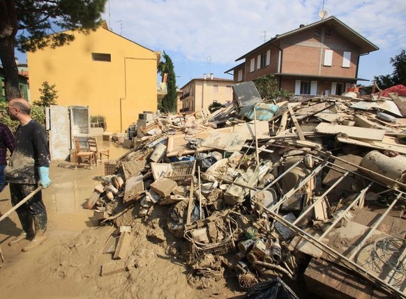 FILE - Volunteers clear mud as household goods are piled on the side of a street in Faenza, Italy, Monday, May 22, 2023. The Italian government has approved more than 2 billion euros ($2.2 billion) in ...