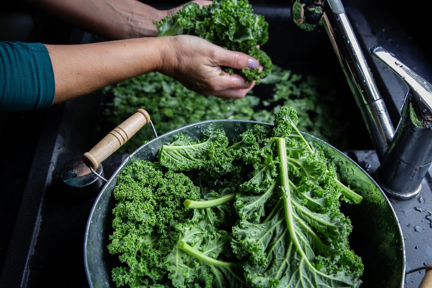 Woman is washing kale leaves with water in the kitchen sink top view on windows light