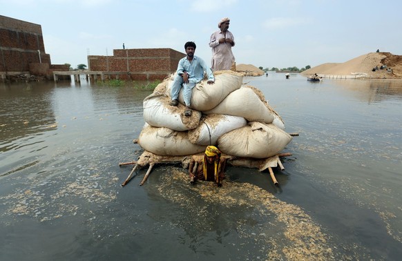 ARCHIV - 05.09.2022, Pakistan, Jaffarabad: Anwohner befördern Säcke mit Futter für ihr Vieh auf einem behelfsmäßigen Floß durch das Hochwasser nach heftigen Monsunregen. Foto: Fareed Khan/AP/dpa +++ d ...