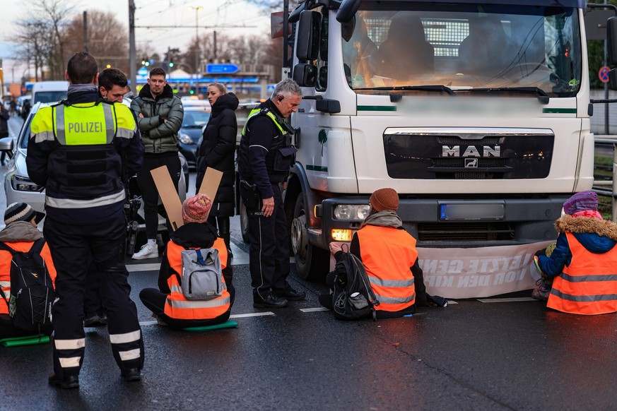 17.01.2023, Nordrhein-Westfalen, Köln: Polizisten sprechen mit Aktivisten der Umweltschutzorganisation Letzte Generation, die vor Fahrzeugen auf einer Straße sitzen. Die Aktivisten haben sich auf eine ...
