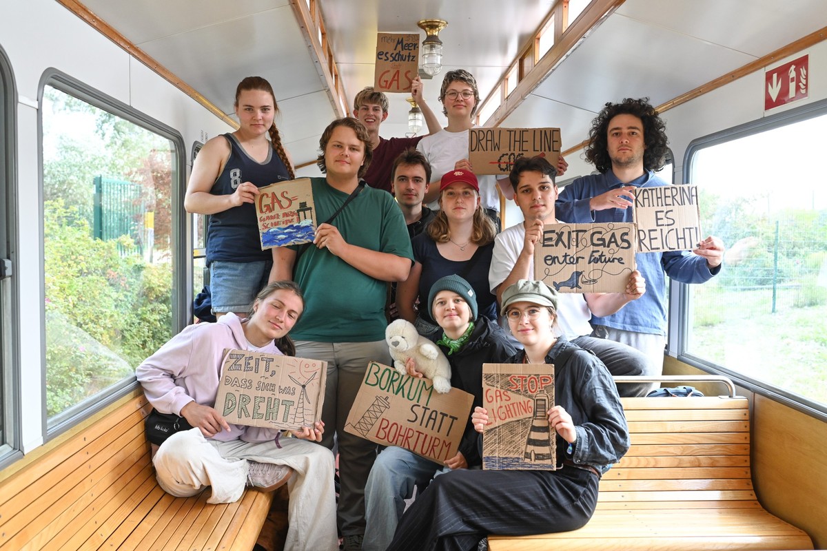04.09.2025, Niedersachsen, Borkum: Aktivisten der Klimabewegung Fridays for Future halten Protestschilder während der Fahrt mit der Inselbahn hoch. Mit einem «Klimacamp» wollen Fridays for Future und  ...