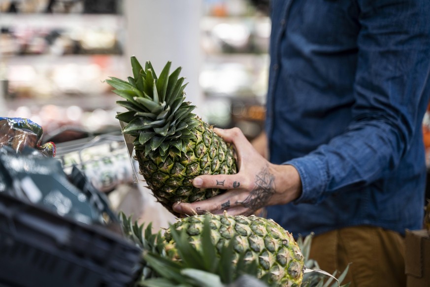 Midsection of mid adult man buying pineapple in supermarket model released Symbolfoto property released AFVF07950