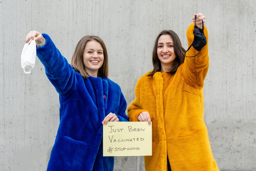 two young girls throwing facemasks after just receiving their covid19 vaccination, urgency to achieve protection for the vulnerable, herd protection