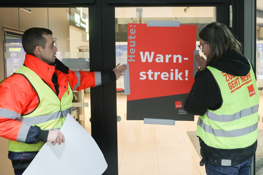 16.02.2023, Hamburg: Airport-Mitarbeiter bringen zu Streikbeginn am Flughafen Hamburg ein Plakat mit der Aufschrift &quot;Warnstreik&quot; an. Die Gewerkschaft Verdi hatte angek