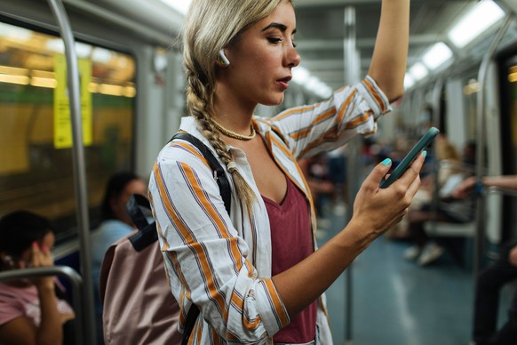 Young blond woman standing in a subway train while using her cellphone