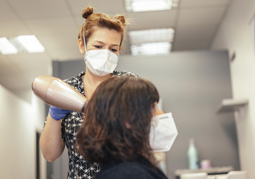 Hairdresser with security measures for the covid-19, new normality, social distance. Drying the hair of a client with a mask