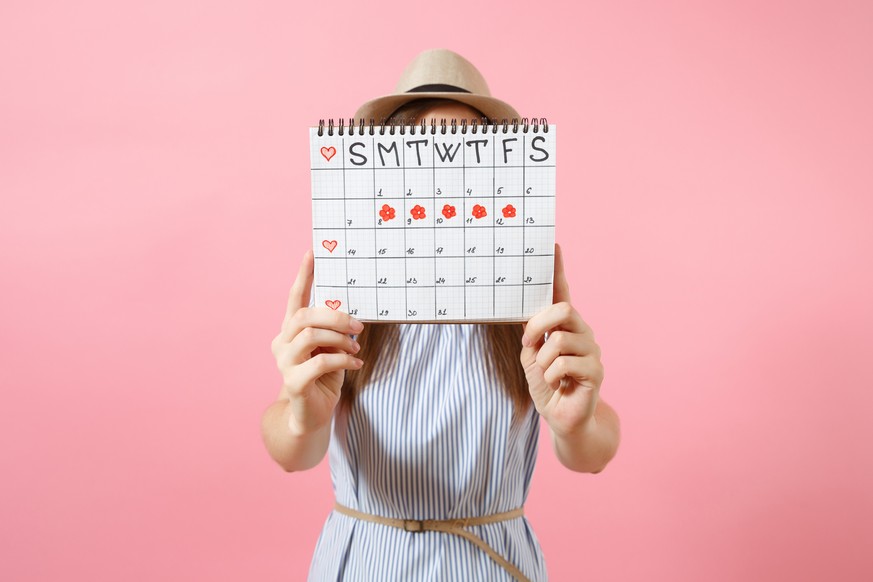 Portrait of woman in blue dress cover face, hiding behind periods calendar for checking menstruation days isolated on trending pink background. Medical, healthcare, gynecological concept. Copy space