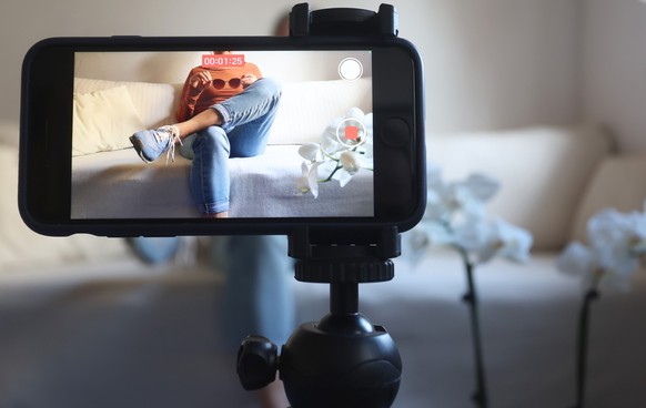 ARCHIV - 08.03.2023, Bayern, Kaufbeuren: Eine Frau sitzt mit einer Sonnenbrille in H�nden auf einem Sofa und filmt sich dabei mit ihrem iPhone (gestellte Szene). Produkttipps auf Instagram oder Tiktok ...