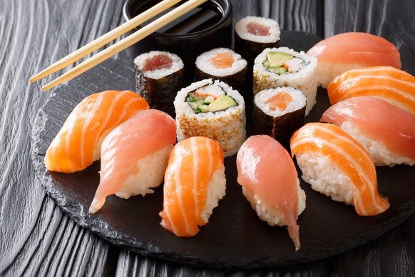 set of sushi and rolls with salmon and tuna, avocado, california, maki, soy sauce, chopsticks close-up on a black stone board on a table. horizontal