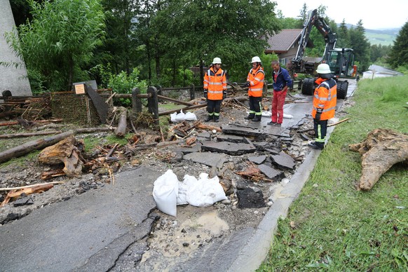 Nach starken Regenfällen begutachten Feuerwehrleute eine durch Wassermassen beschädigte Straße im Ortsteil Kranzegg.