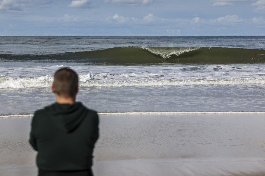 28.09.2022, Schleswig-Holstein, Westerland/Sylt: Ein Mann schaut am Brandenburger Strand auf eine brechende Welle. Foto: Frank Molter/dpa +++ dpa-Bildfunk +++