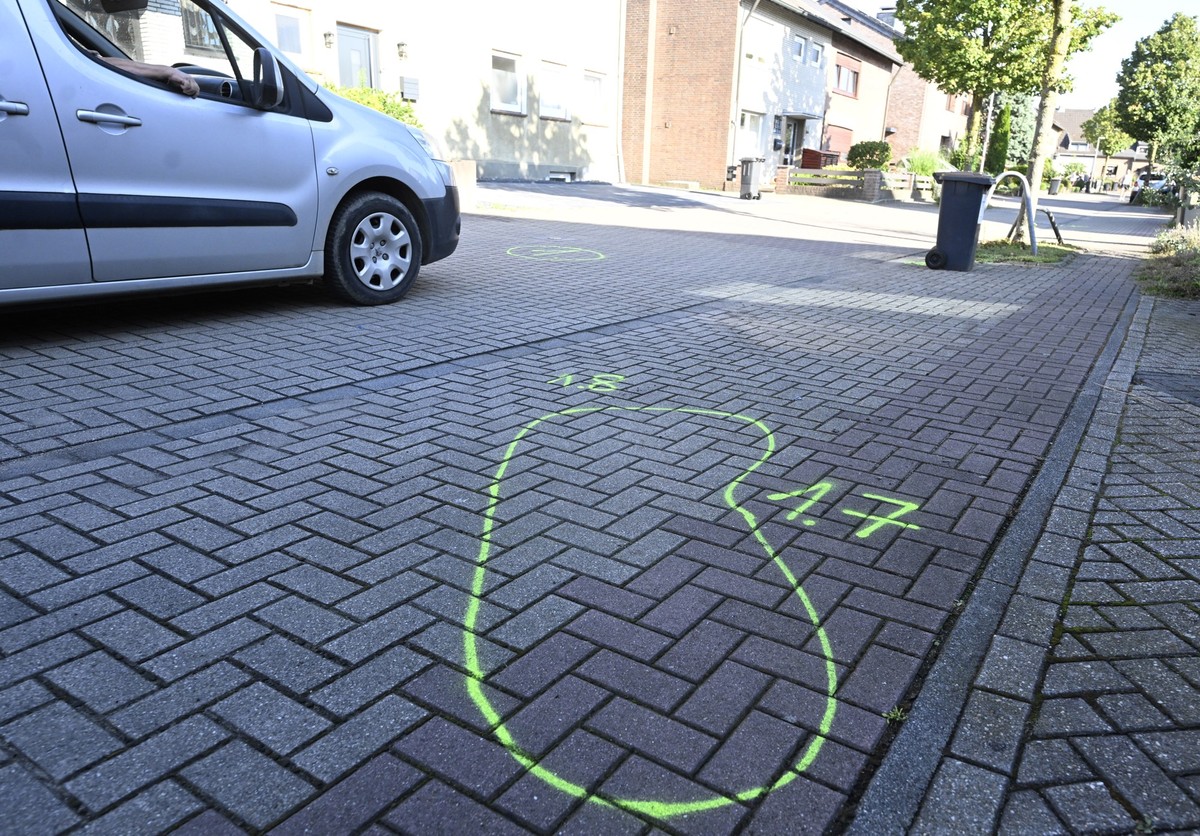 28.08.2024, Nordrhein-Westfalen, Moers: Ein Auto fährt am Tatort im Norden von Moers an der auf dem Gehweg markierten Spurensicherung vorbei, die die Lage des Angreifers anzeigt. Im niederrheinischen  ...
