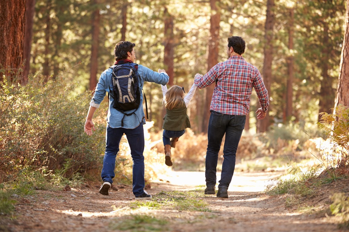Gay Male Couple With Daughter Walking Through Fall Woodland