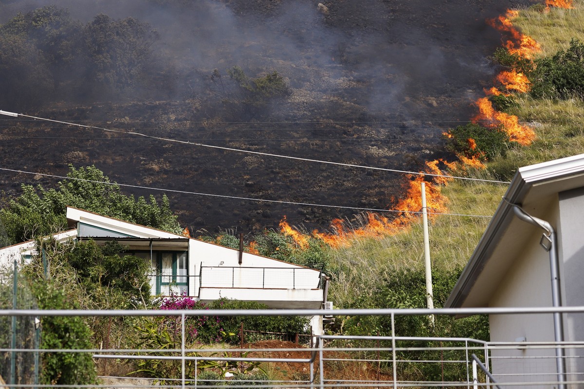 25.07.2023, Italien, Capaci: Ein Feuer breitet sich auf einer Fläche hinter einem Wohnhaus in der Nähe von Palermo aus. Auf der italienischen Mittelmeerinsel Sizilien sind größere Wald- und Flächenbrä ...