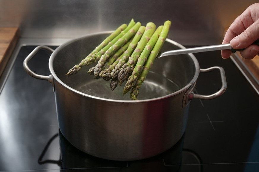 Hand puts green asparagus on a skimmer in a pot with boiling water for a holiday dinner, healthy cooking concept, copy space, selected focus, narrow depth of field