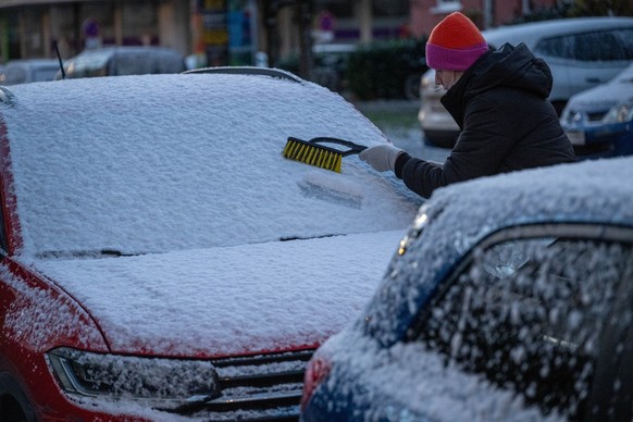 25.11.2023, Bayern, München: Eine Frau befreit am frühen Morgen ein Auto von Schnee und Eis. Auch in den kommenden Tagen soll es winterlich bleiben. Foto: Stefan Puchner/dpa +++ dpa-Bildfunk +++