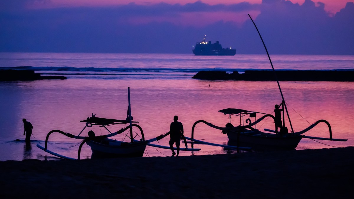 ARCHIV - 14.11.2022, Indonesien, Nusa Dua: Männer befestigen vor Sonnenaufgang am Tag vor Beginn des G20-Gipfels am Strand von Nusa Dua Boote, wobei im Hintergrund ein Schiff der indonesischen Marine ...