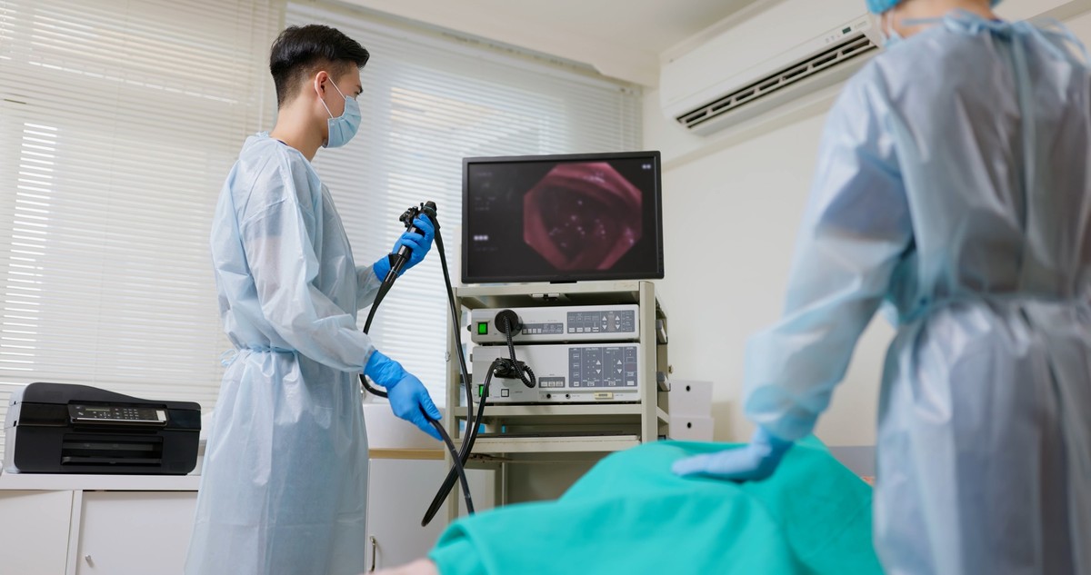 asian male doctor wearing protective gown are doing colonoscopy for elderly man while nurse comforting patient in hospital