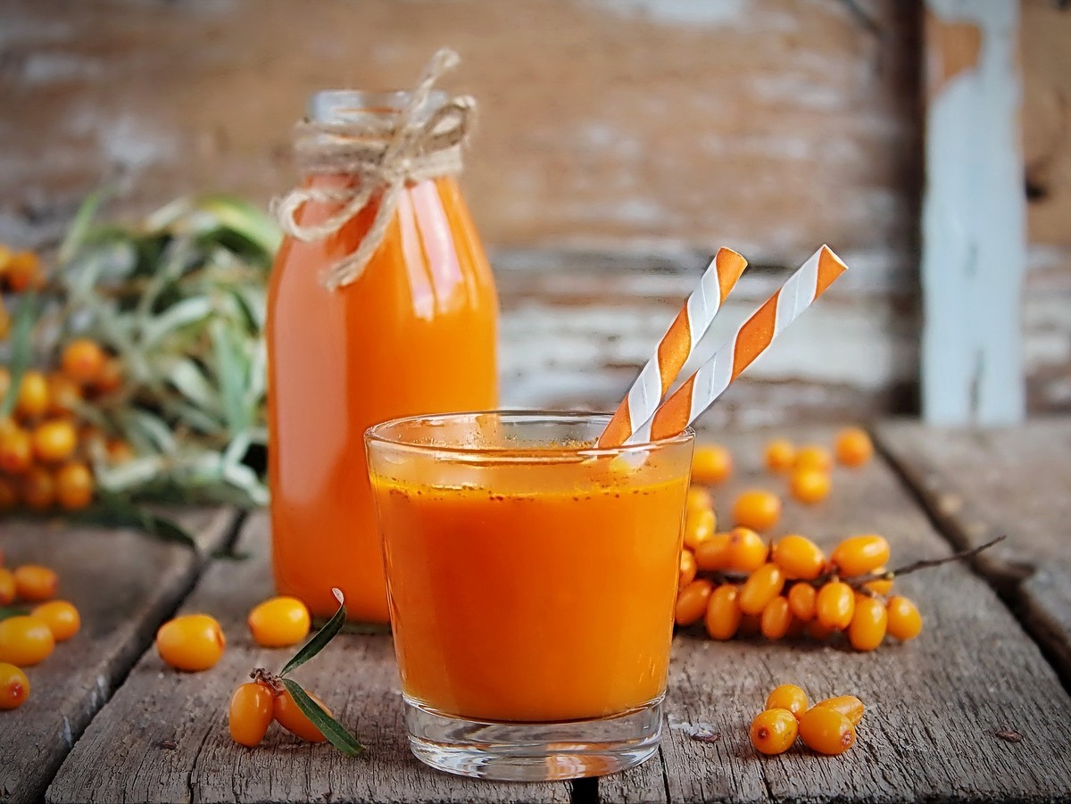 Homemade buckthorn soft drink in a glass and ripe sea buckthorn berries on the table. Healthy and diet food