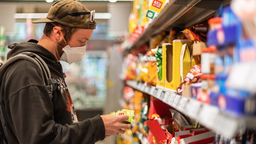 20.04.2020, Sachsen, Dresden: Ein Kunde steht in einem Supermarkt vor einem Regal, und trägt dabei einen Mundschutz. Am heutigen Montag werden die ersten Corona-Auflagen schrittweise gelockert, in Sac ...