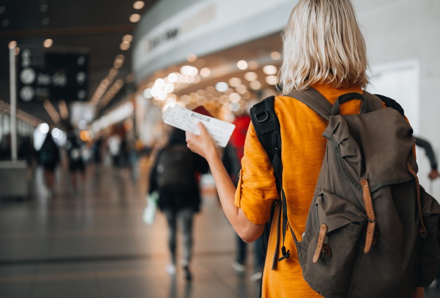 Rear view of a woman at the airport holding a passport with a boarding pass as she walks to her departure gate