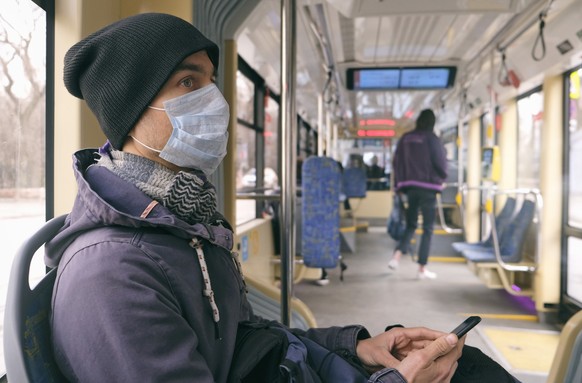 Adult man with medical protective mask and gloves inside public transport tram using smartphone. Disease outbreak, coronavirus covid-19 pandemic, virus protection, air pollution.
