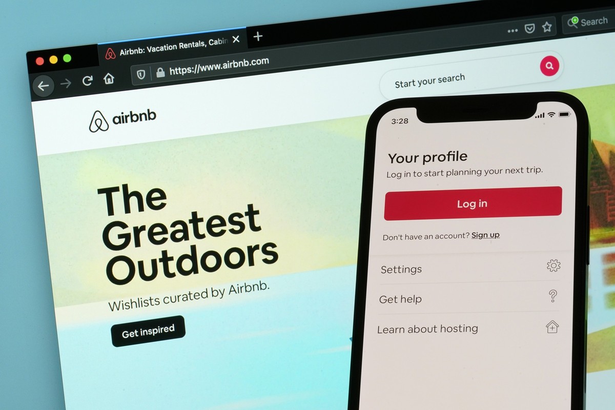 FILE - The login page for Airbnb's iPhone app is seen in front of a computer displaying Airbnb's website on May 8, 2021, in Washington. Airbnb is going back to its roots to cater to traveler ...