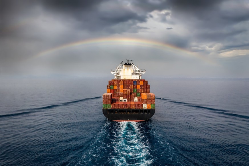 Aerial view of a container cargo ship sailing into bad weather with a rainbow in the cloudy sky