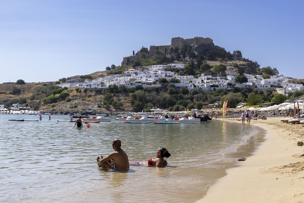 ARCHIV - 26.07.2023, Griechenland, Lindos: Am Strand in Lindos, etwa 10 Kilometer von den Br�nden im S�dosten entfernt, sind weiterhin Touristen am Strand, im Hintergrund die weltbekannte Akropolis vo ...