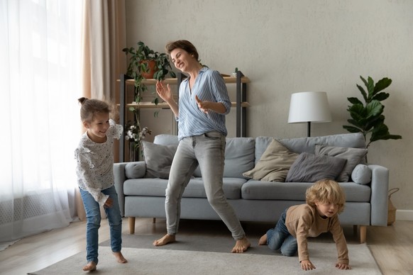 Happy mom and two cheerful sibling kids having fun at home, dancing to music, enjoying activities, laughing, exercising, playing. Nanny, sitter watching children in living room. Family leisure Single- ...