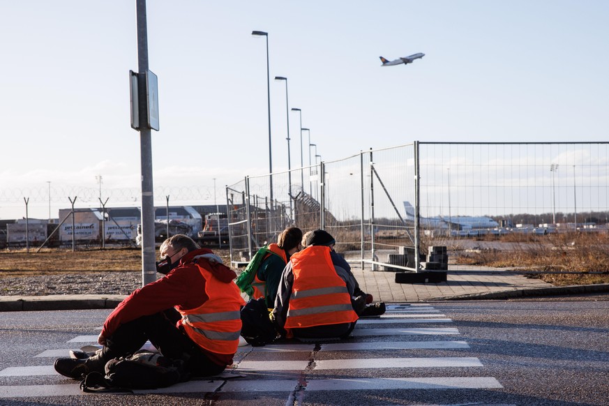 Aktivisten der Gruppe „Die letzte Generation“ haben sich mit ihren Händen auf einen Zebrastreifen auf der Südallee, einer Zufahrt zum Frachtbereich vom Münchner Flughafen, geklebt.