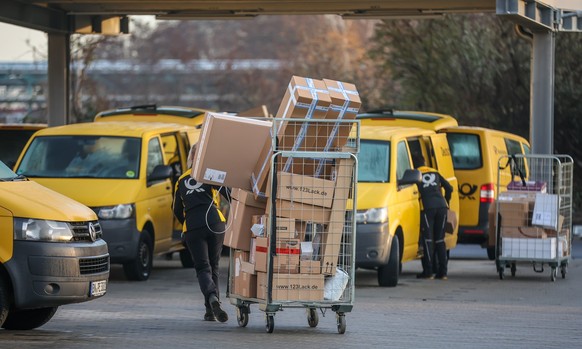 ARCHIV - 25.11.2022, Sachsen-Anhalt, Bitterfeld-Wolfen: Eine Mitarbeiterin der Deutsche Post DHL zieht einen vollen Paketwagen zu ihren Fahrzeug über den Hof eines Zustellpunktes. (zu dpa: «Die Post b ...