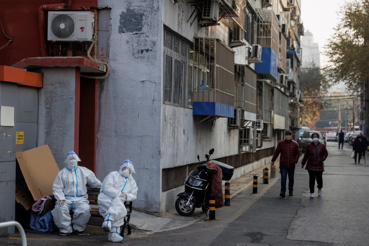 Epidemic prevention workers in protective suits sit in a locked-down residential compound as outbreaks of the coronavirus disease (COVID-19) continue in Beijing, November 23, 2022. REUTERS/Thomas Pete ...