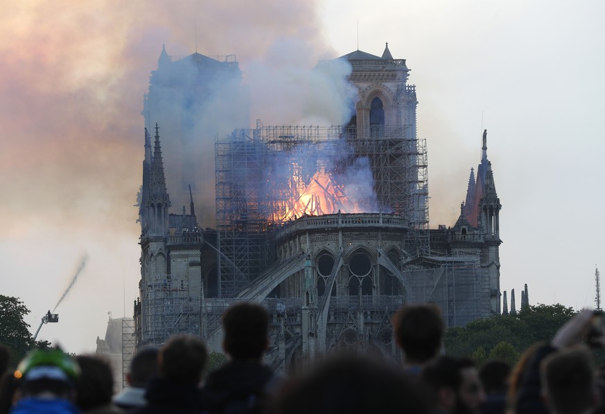 People watch as flames and smoke rise from Notre Dame cathedral as it burns in Paris, Monday, April 15, 2019. Massive plumes of yellow brown smoke is filling the air above Notre Dame Cathedral and ash ...